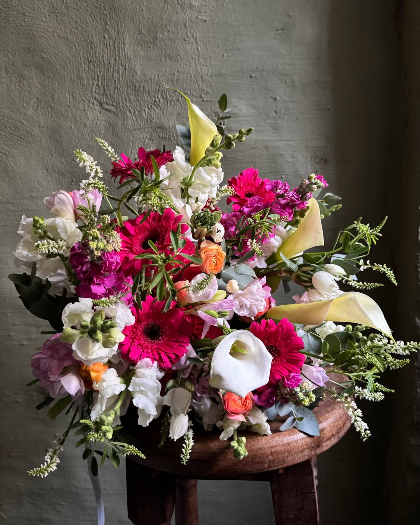 Colorful flower arrangement on a wooden stool against a gray wall
