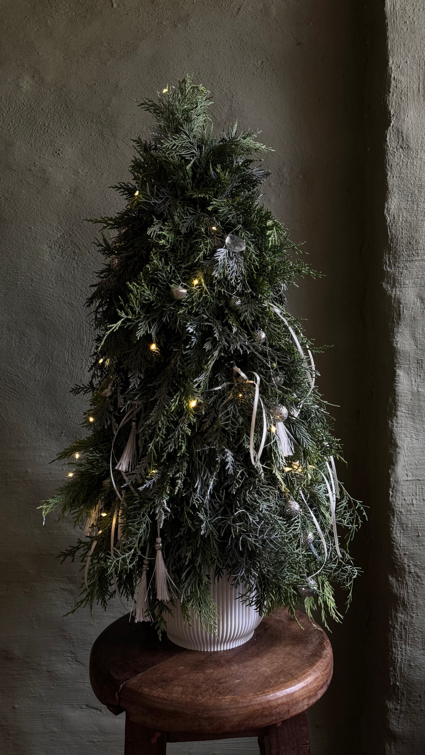 Decorated Christmas tree with lights on a wooden stool against a dark wall