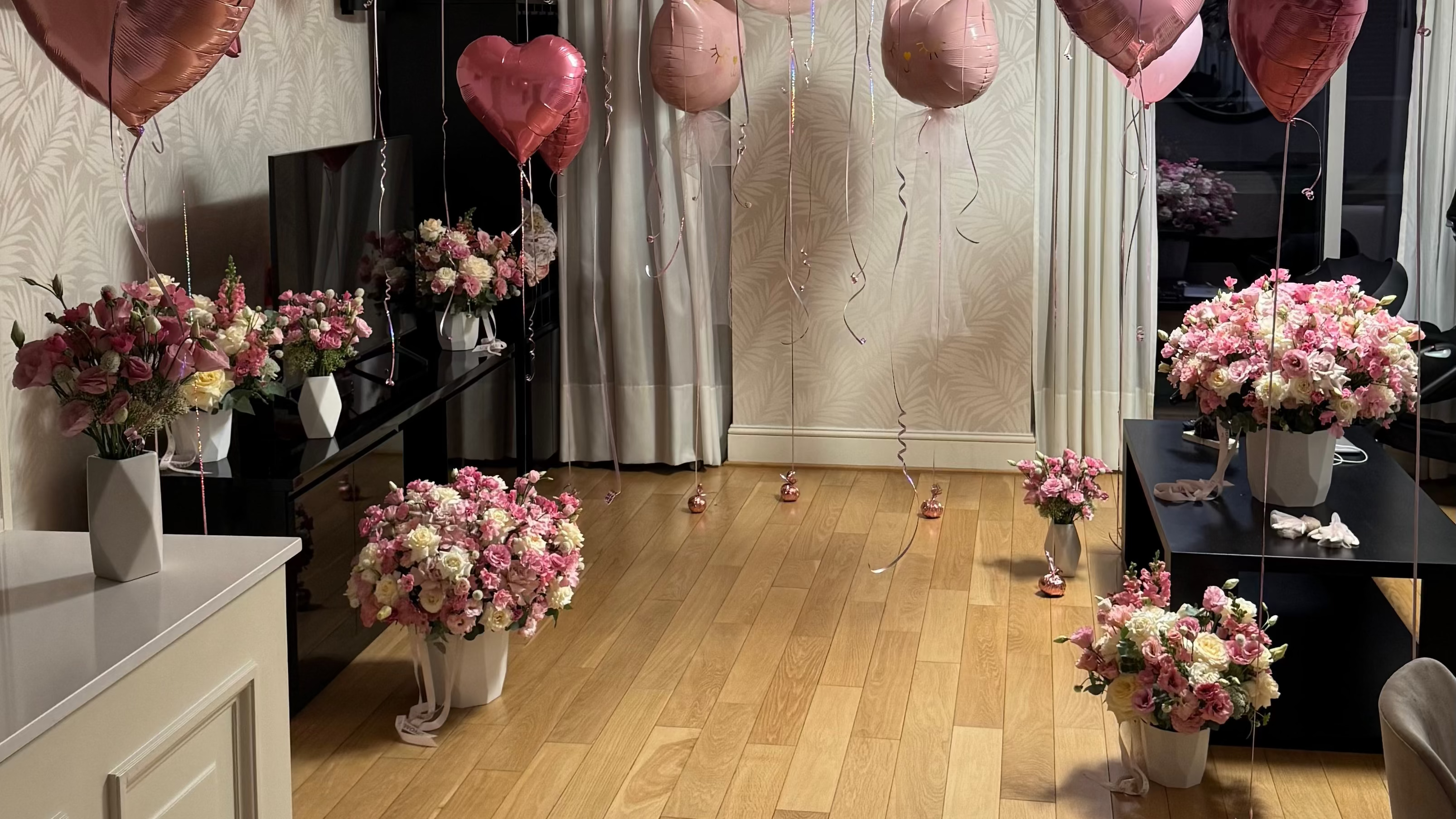 Decorative balloons and flower arrangements in a room with wooden flooring.