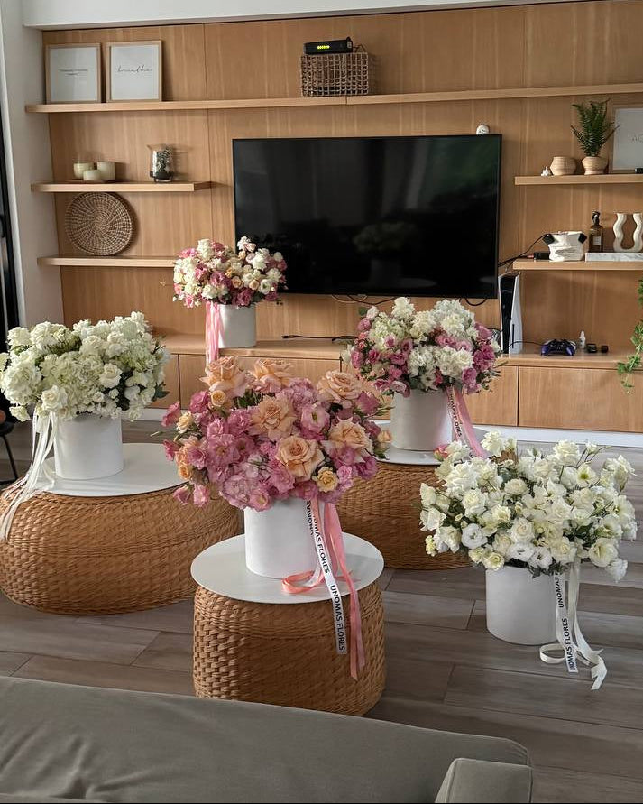 Decorative flowers on small tables in a living room setting with a TV and shelves.