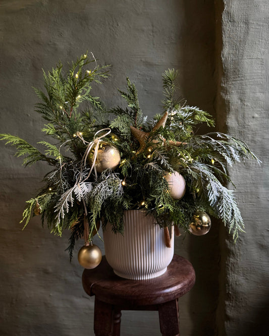 Decorative plant arrangement with gold ornaments on a wooden stool against a textured wall.