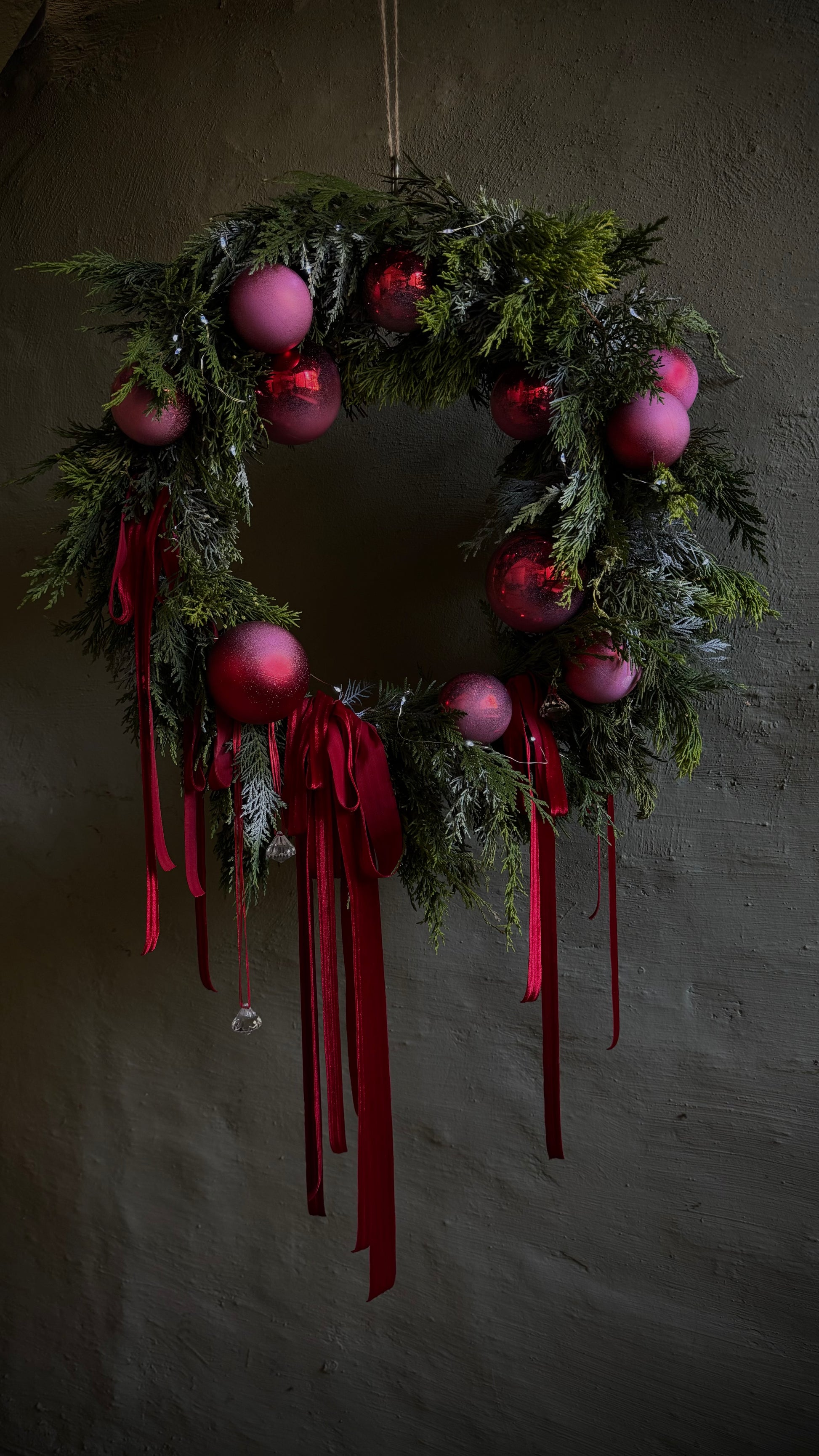 Decorative wreath with pink ornaments and red ribbons on a dark background