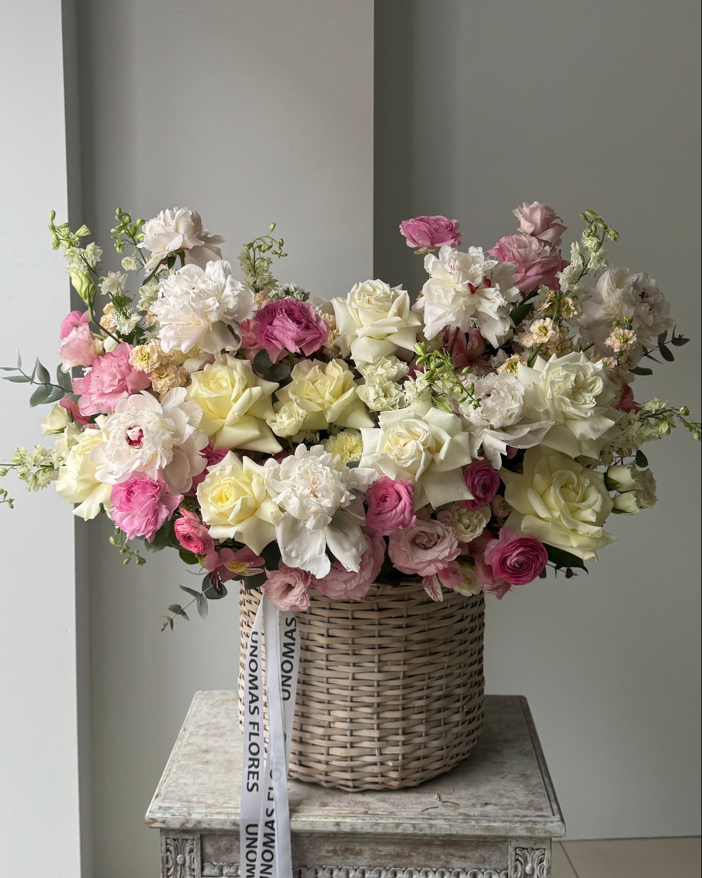 Bouquet of flowers in a woven basket on a wooden table against a gray wall.
