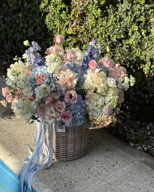 Gran arreglo floral delicado en box de mimbre con hortensias azules, rosas ecuatorianas blancas y rosa claro con pétalos hacia atrás, delphinium violeta y mattiola blanca de Unomas Flores, envío a domicilio en Buenos Aires