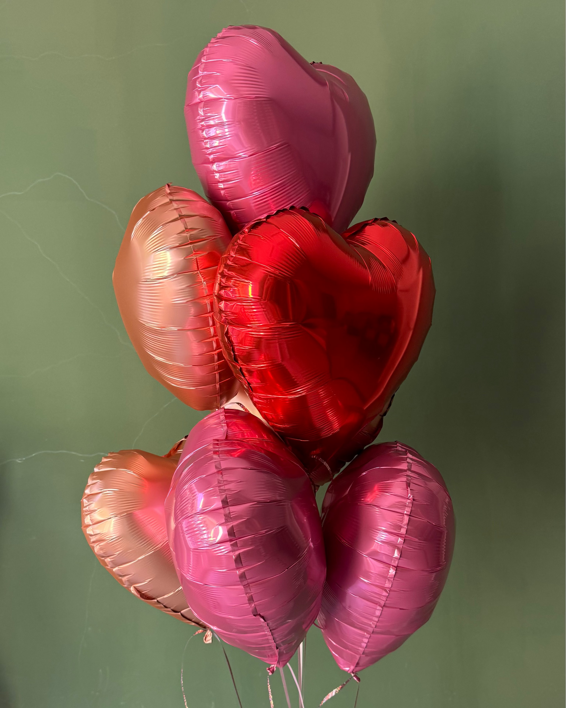 Heart-shaped balloons in red, pink, and gold on a green background