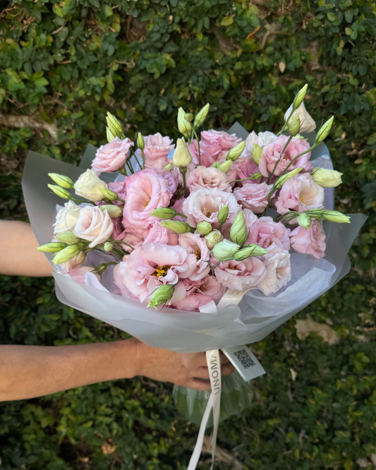Bouquet of pink flowers held by a person against a green leafy background