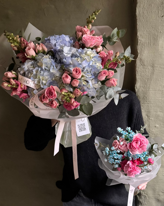Person holding two bouquets of flowers blue and pink against a plain background
