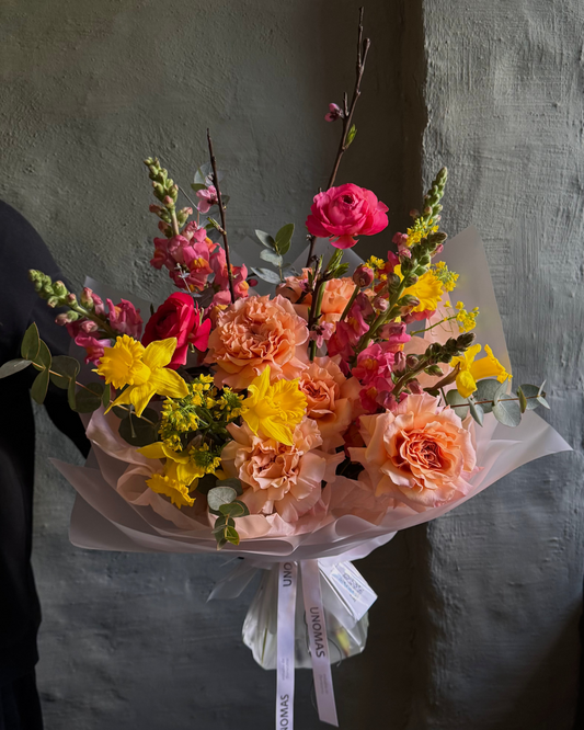 Ramo de flores mixtas en tonos amarillo brillante, naranja y rosa, con rosas ecuatorianas, envuelto para regalo.