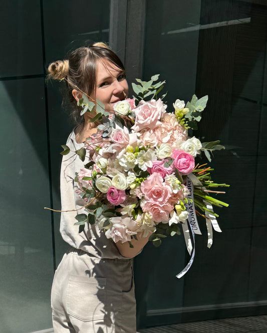 Woman holding a bouquet of pink and white flowers in front of a modern building.
