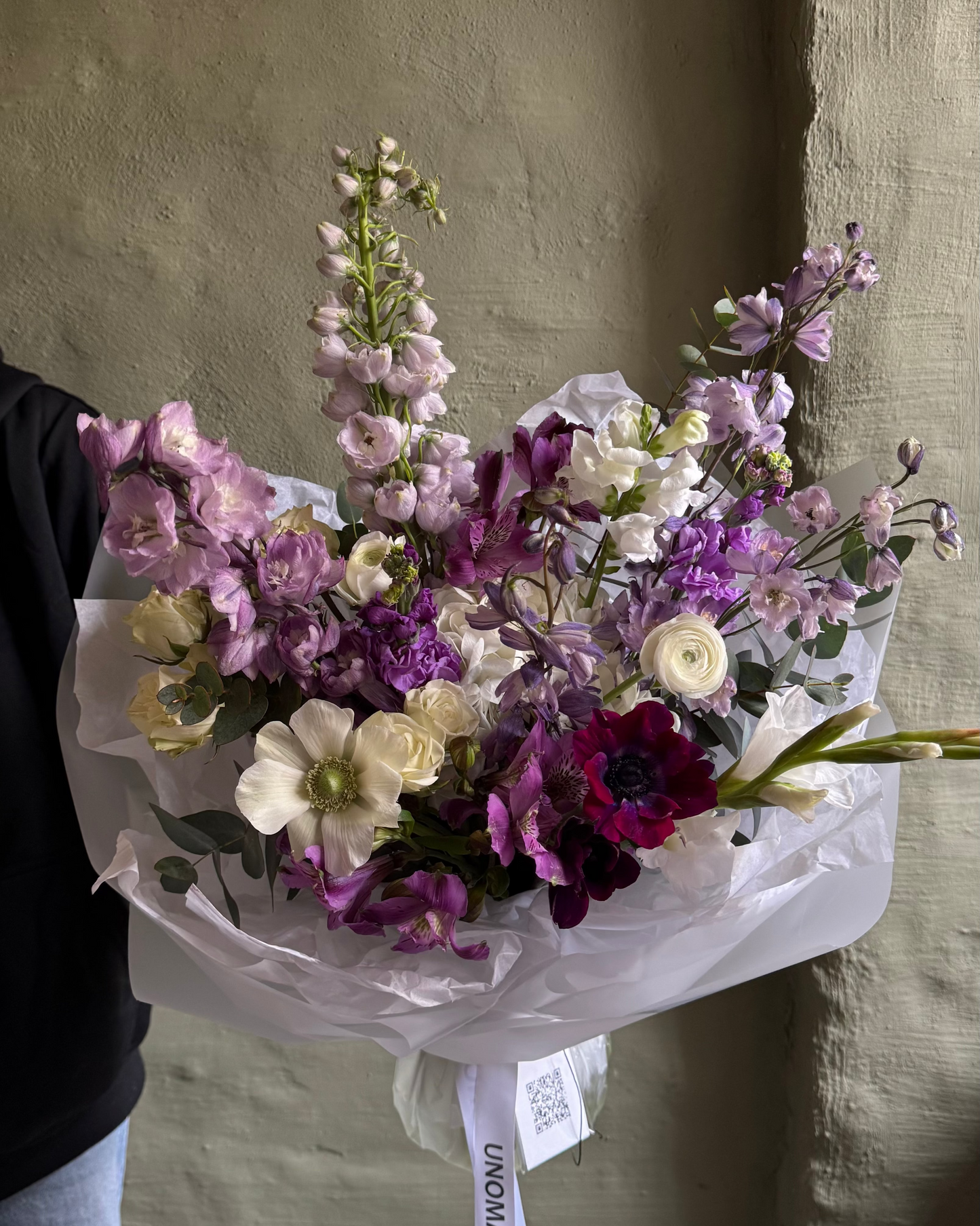 Bouquet of purple and violet flowers held against a plain background