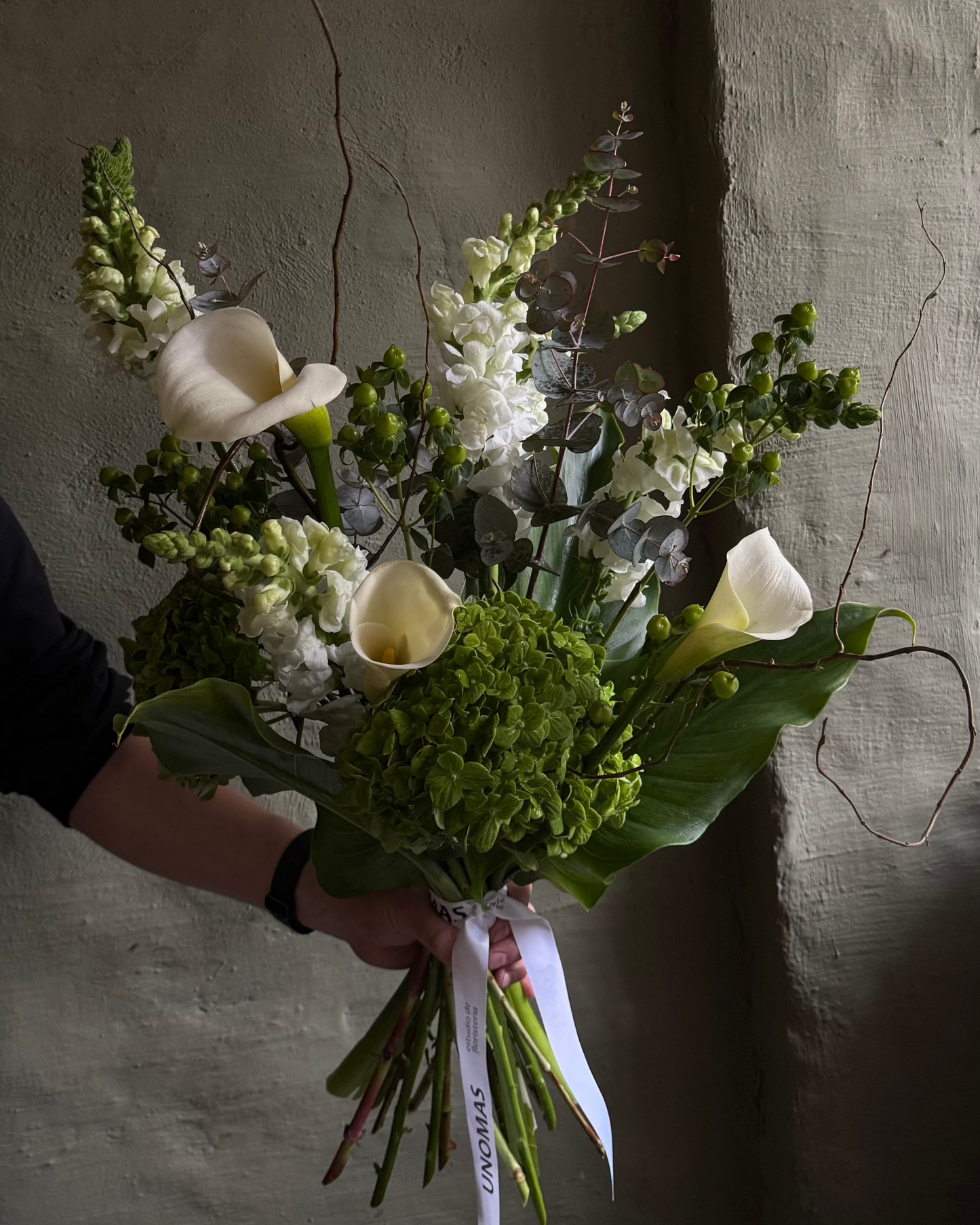 Men bouquet of green flowers held against a textured wall
