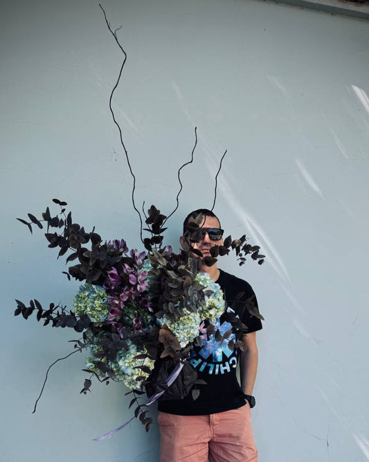 Person holding a large floral arrangement against a light-colored wall.