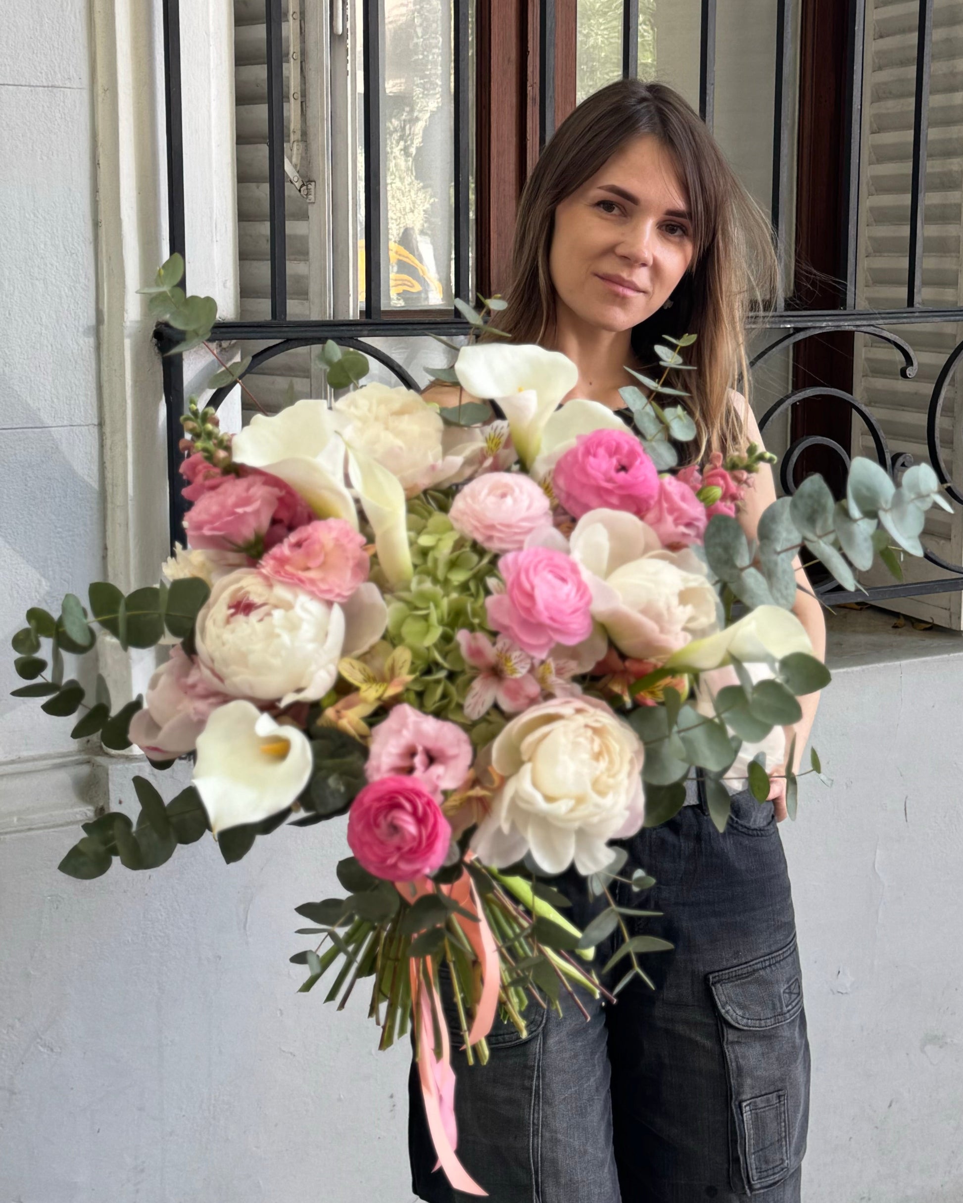 Woman holding a large bouquet of flowers in front of a building entrance.