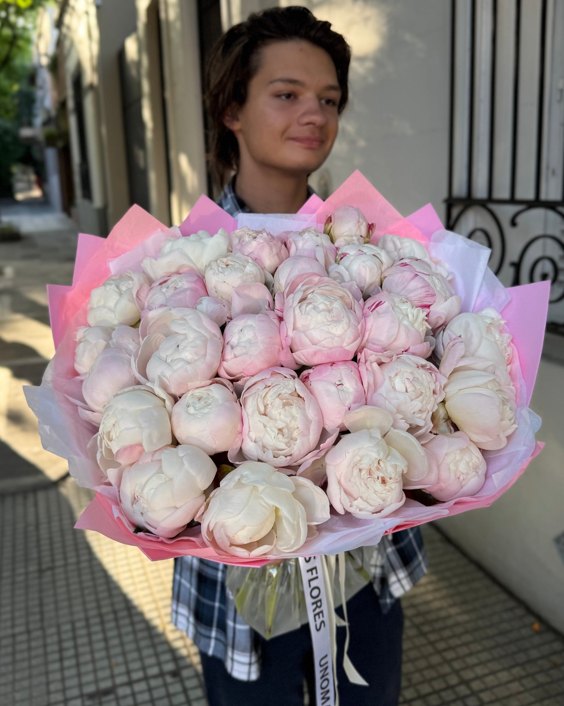 Person holding a large bouquet of white and pink flowers outdoors.