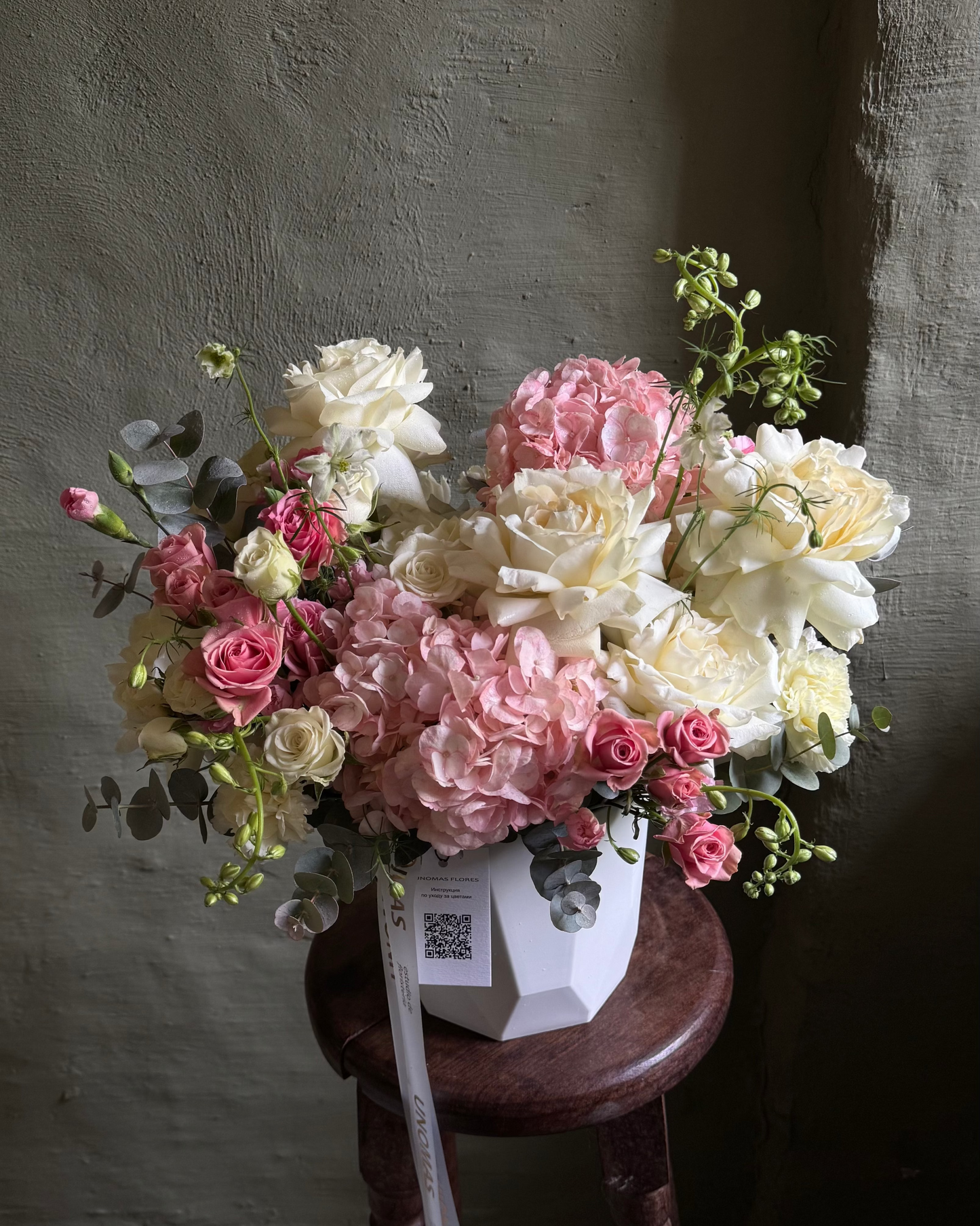 Bouquet of flowers on a wooden stool against a textured wall.