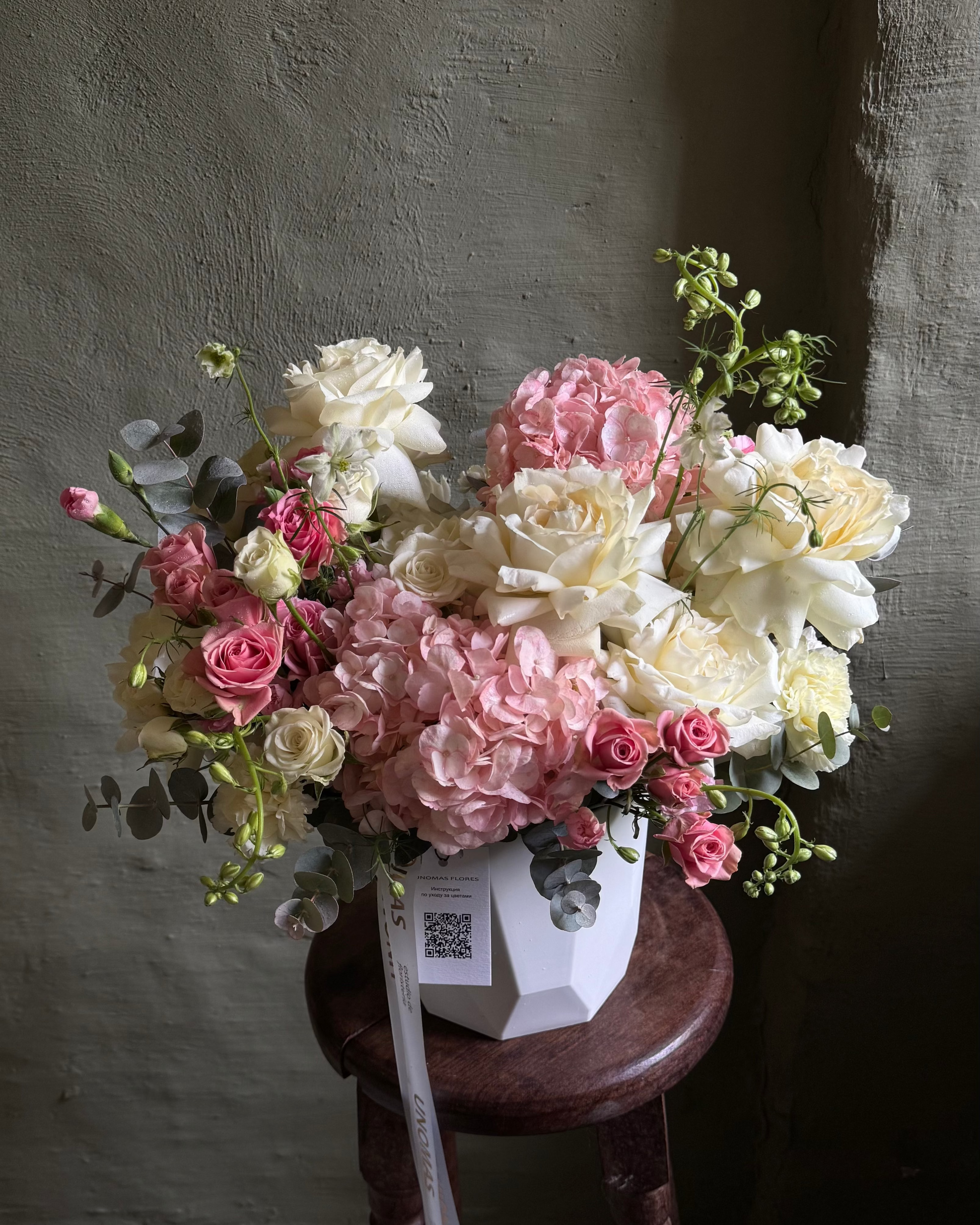 Bouquet of flowers on a wooden stool against a textured wall.