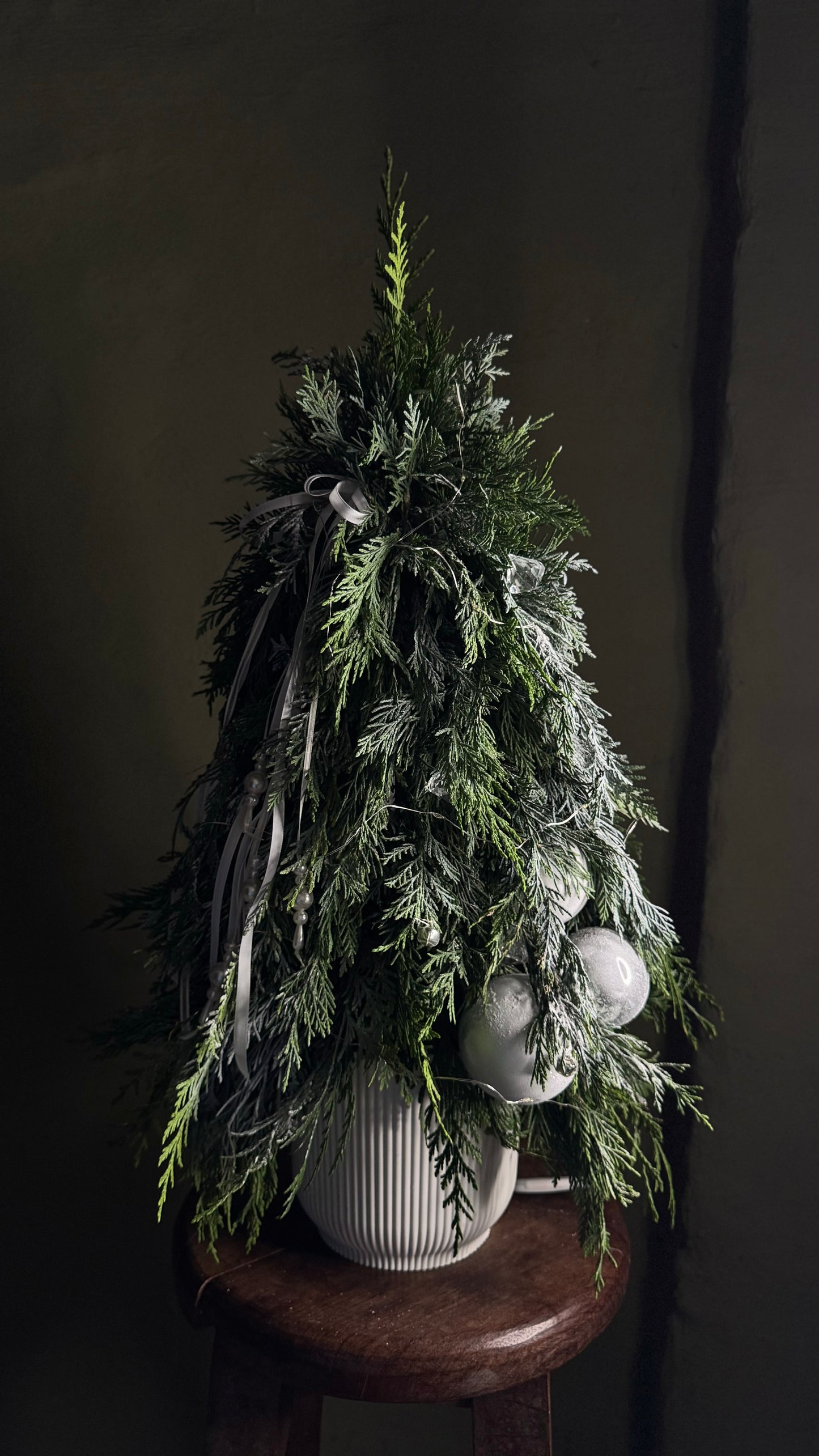 Árbol de Navidad decorado con luces blancas, bolas plateadas y cintas en un cachepot blanco