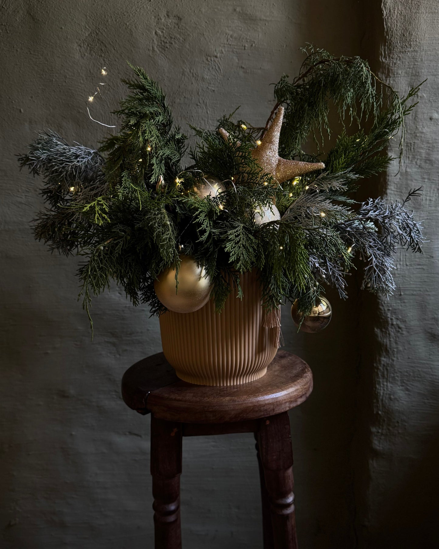 Decorative arrangement of greenery with gold ornaments on a wooden stool against a textured wall.