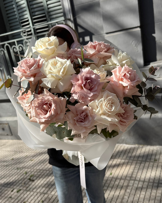 Person holding a bouquet of pink and white roses on a sidewalk.