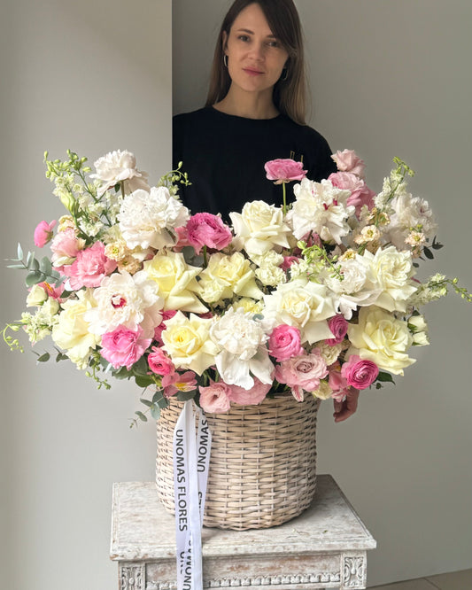 Woman holding a large bouquet of flowers in a wicker basket on a small table.