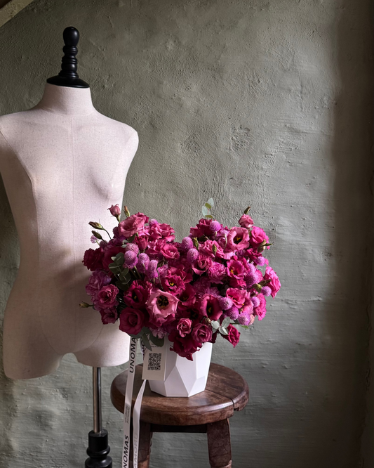 Mannequin torso with pink flowers on a wooden stool against a textured wall.
