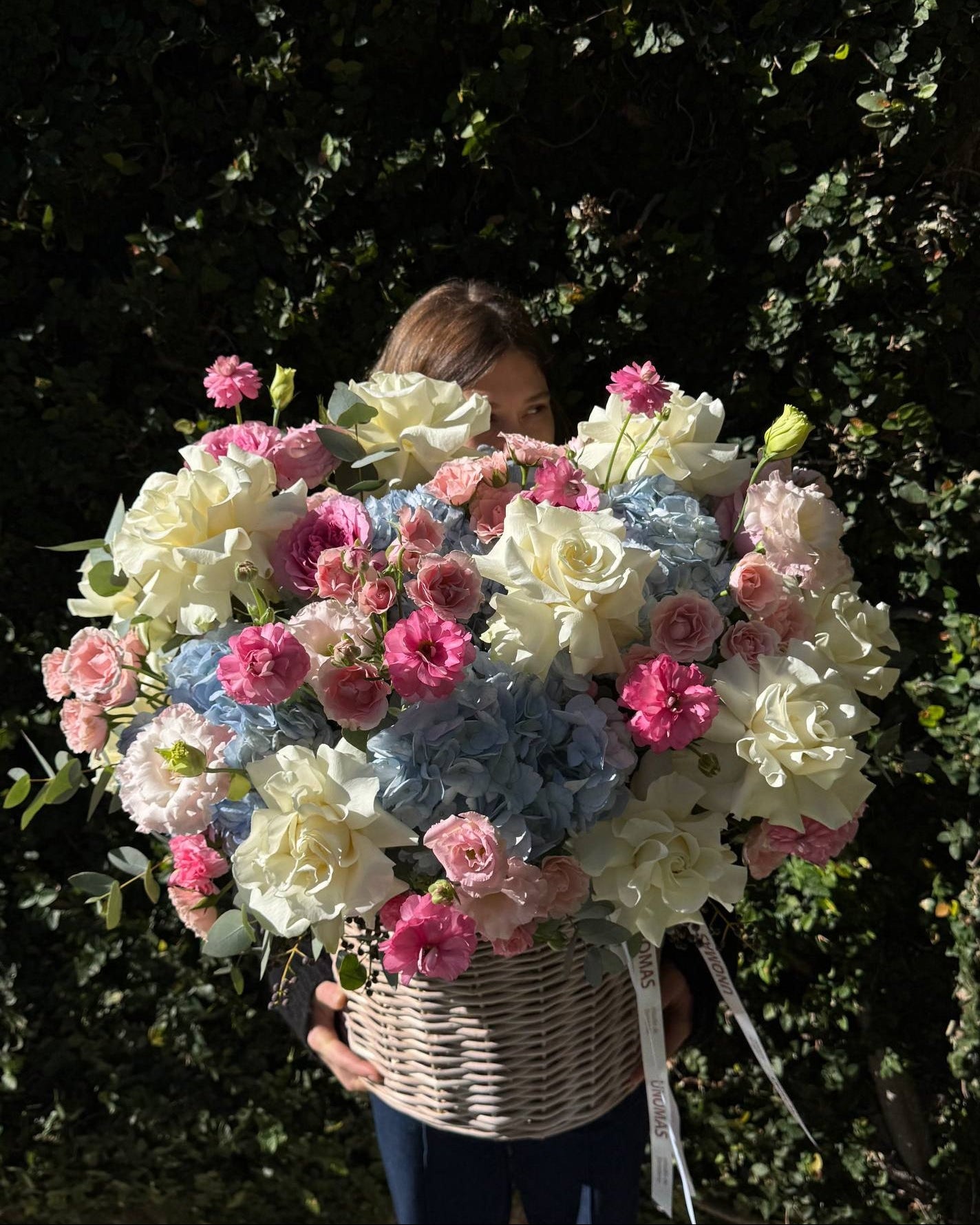 Person holding a large bouquet of flowers in front of a green hedge