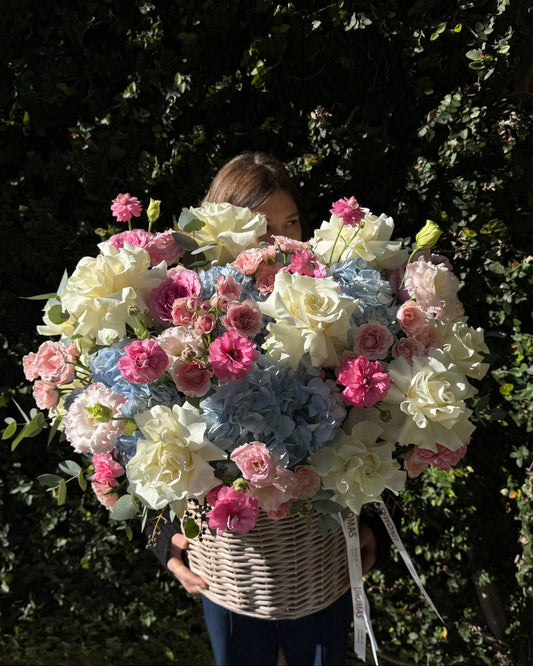 Person holding a large bouquet of flowers in front of a green hedge