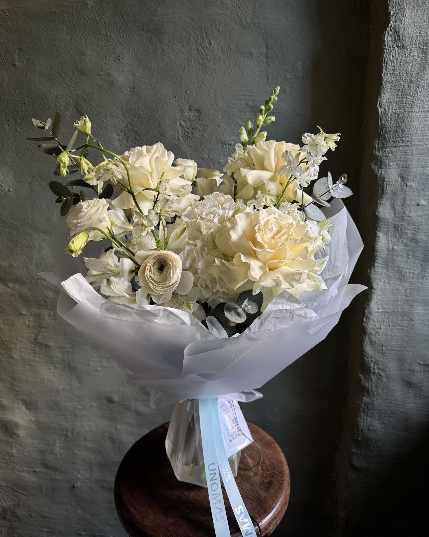 Un ramo de flores blancas y crema envuelto en papel blanco translúcido con una cinta celeste de Unomas Flores, envío a domicilio en Buenos Aires