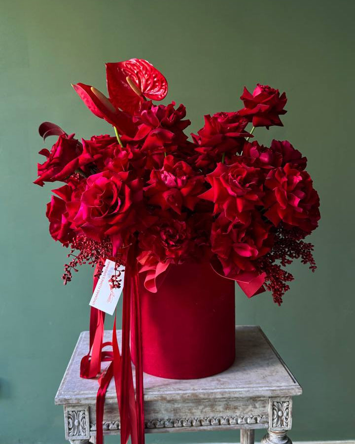 Red floral arrangement in a matching red box on a white table against a green wall.