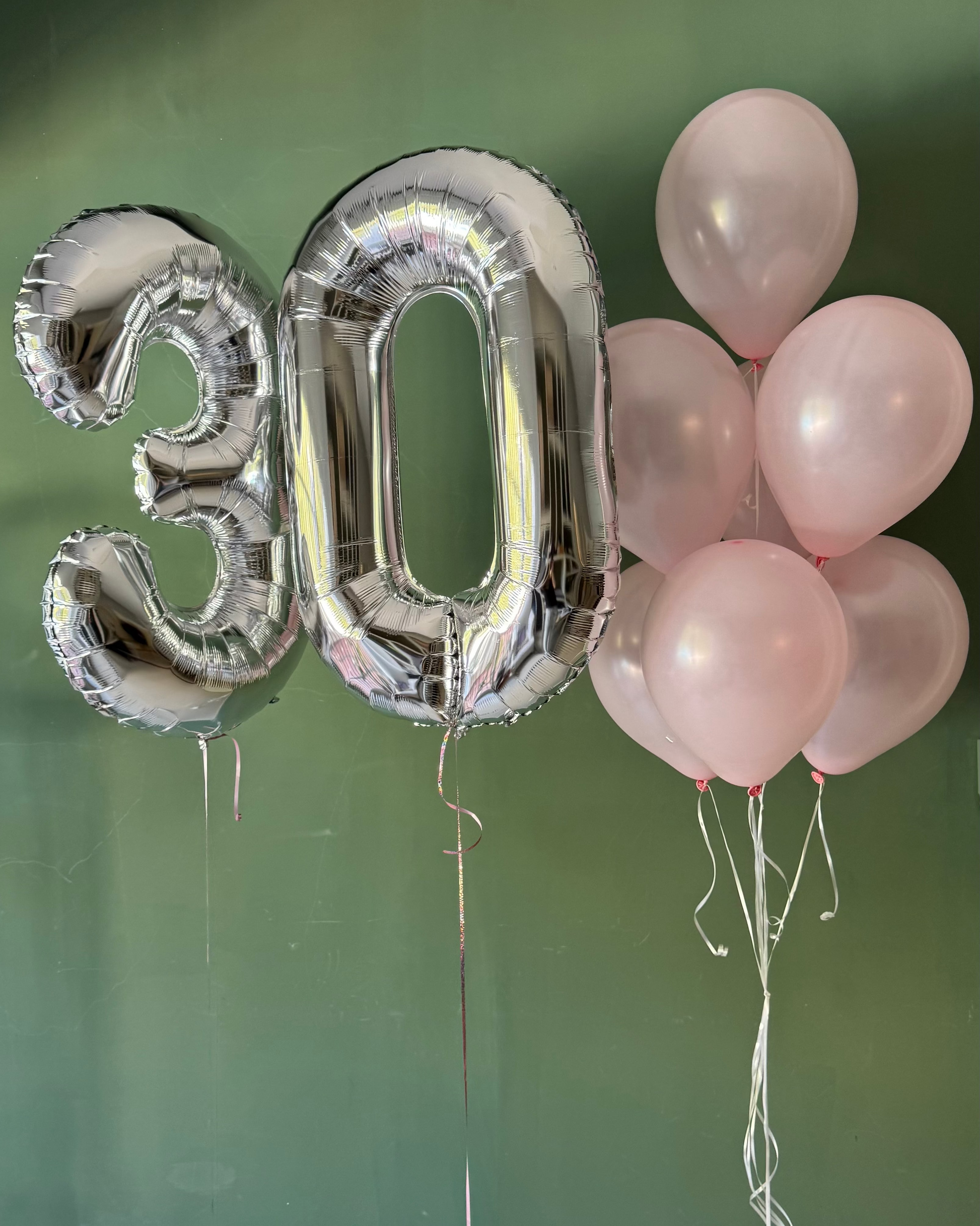 Silver '30' balloons and pink balloons against a green wall.