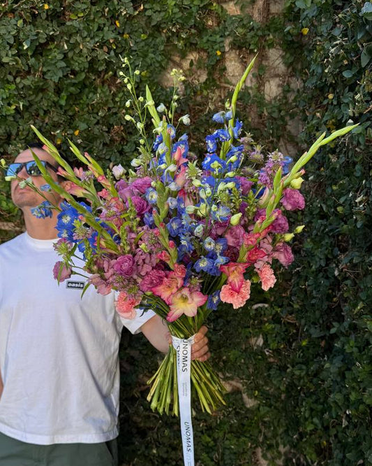 Person holding a large bouquet of colorful flowers against a green leafy background