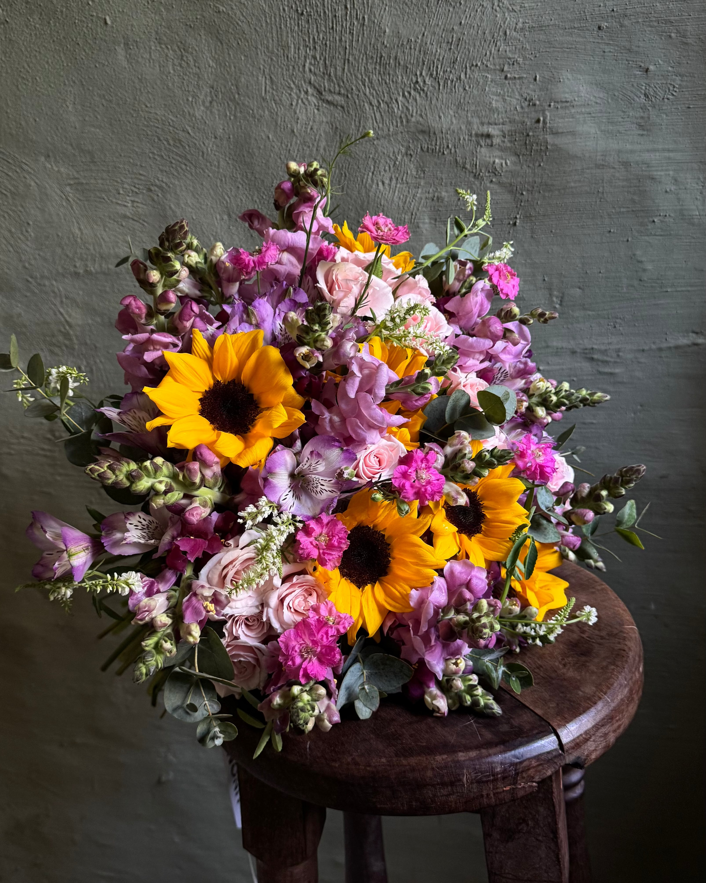 Bouquet of flowers with sunflowers on a wooden stool against a dark background