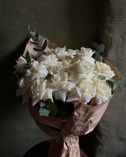 A bouquet of white reflexed roses wrapped in kraft paper with eucalyptus leaves.