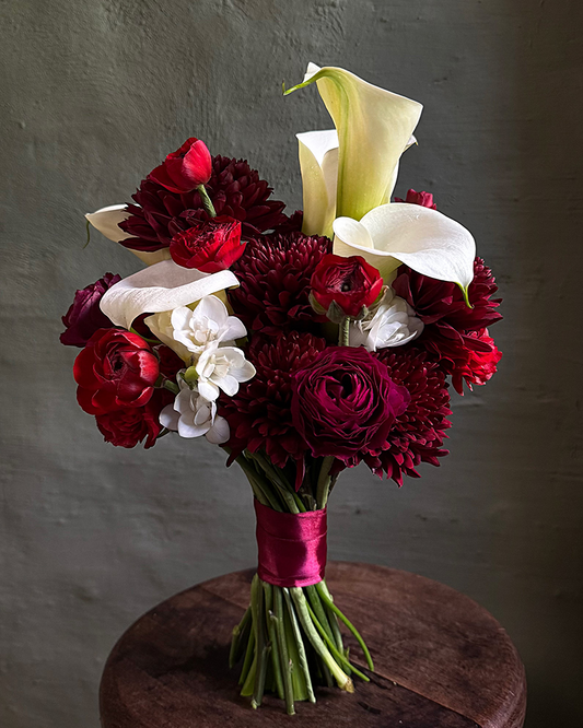 Bouquet of red, white, and burgundy flowers on a wooden stool against a dark background