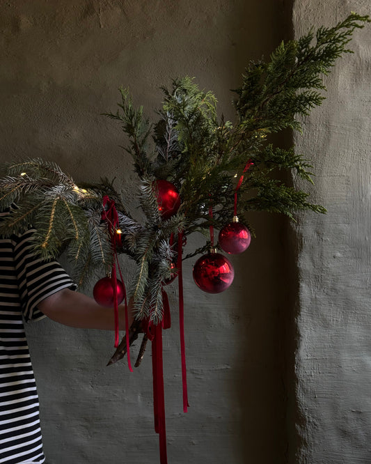 Person holding a decorative branch with red ornaments against a textured wall.