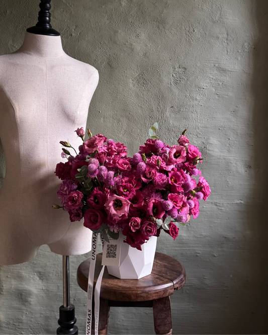Mannequin torso with pink flowers on a wooden stool against a textured wall.
