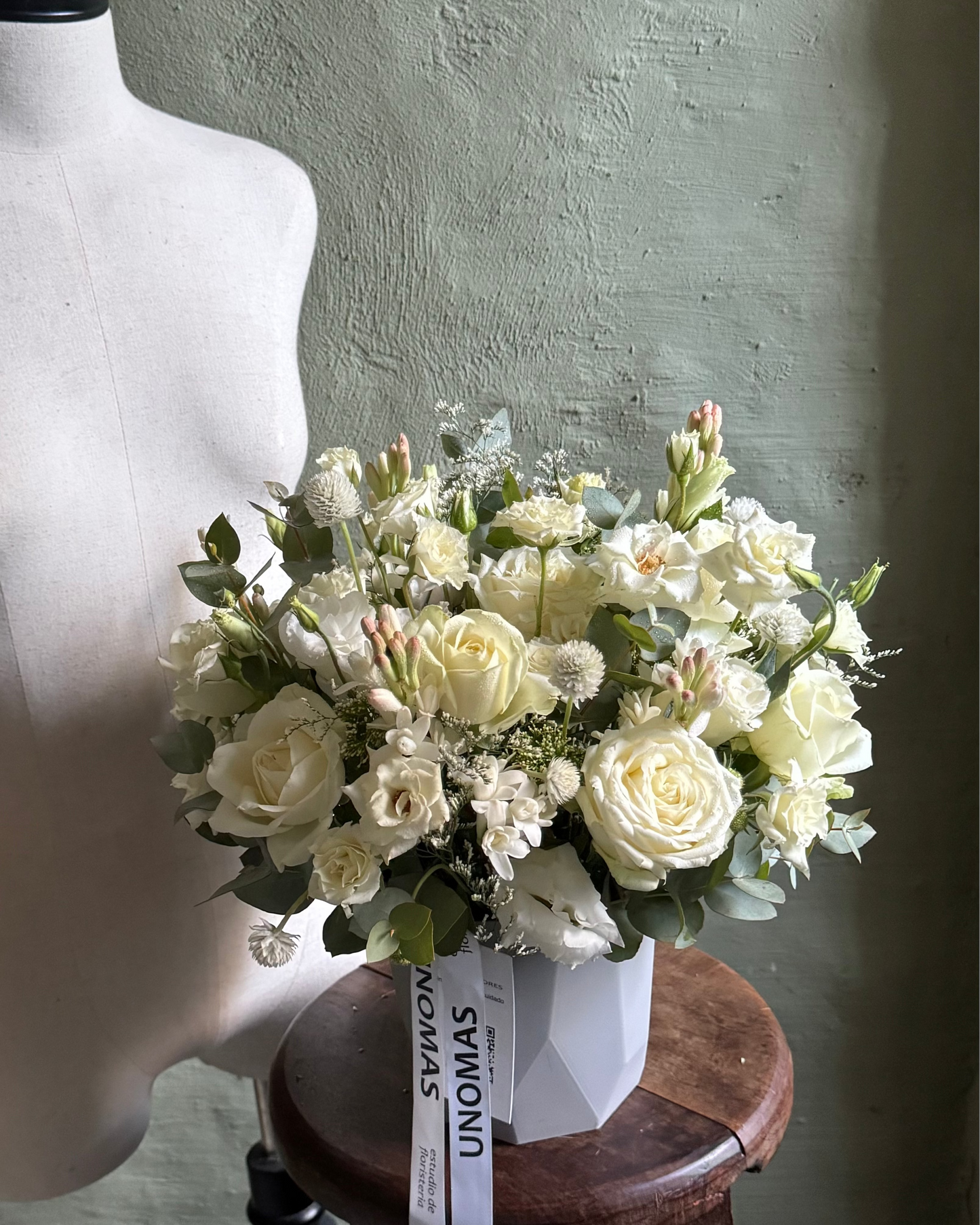 Bouquet of white flowers on a wooden stool against a textured wall.