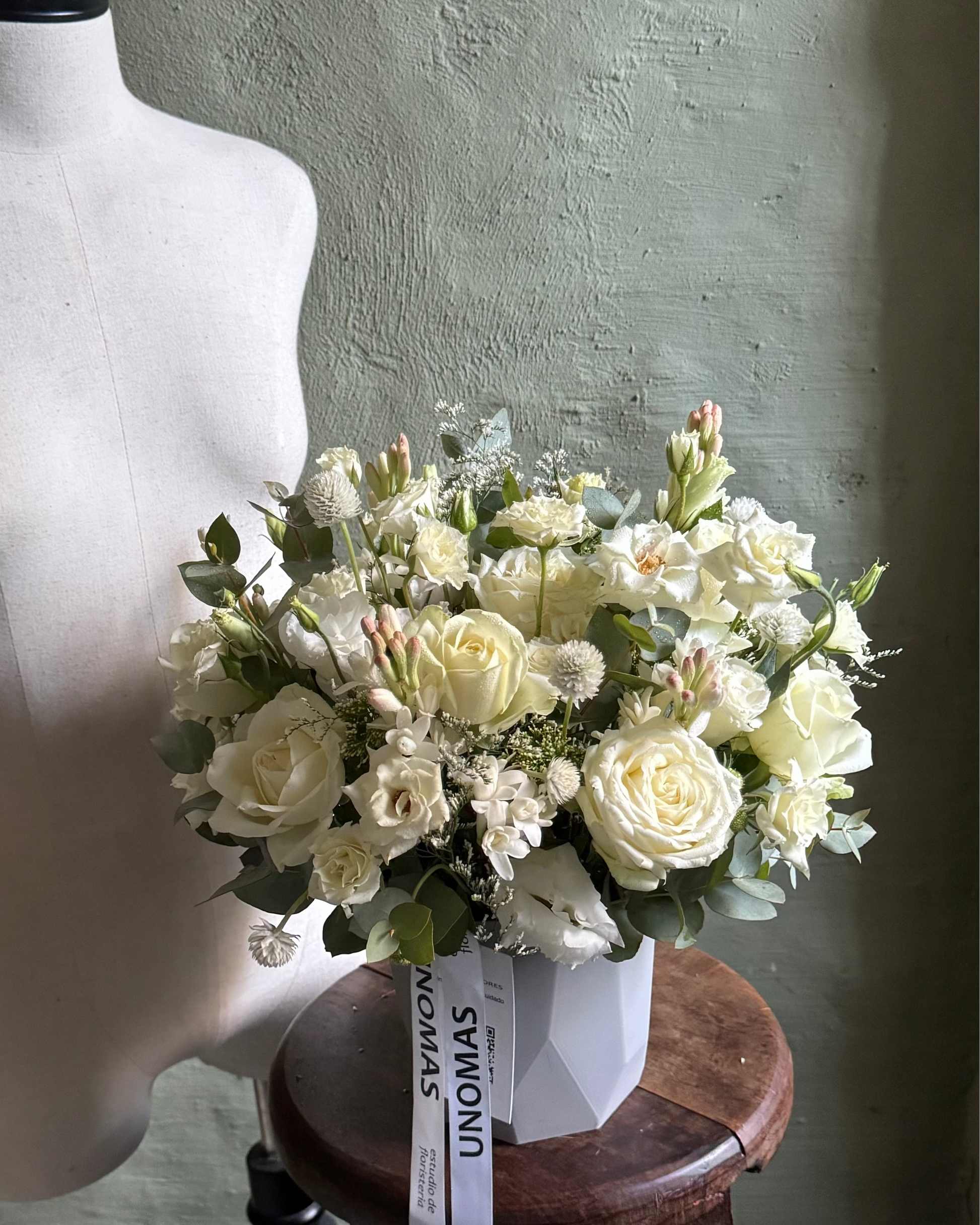 Bouquet of white flowers on a wooden stool against a textured wall.