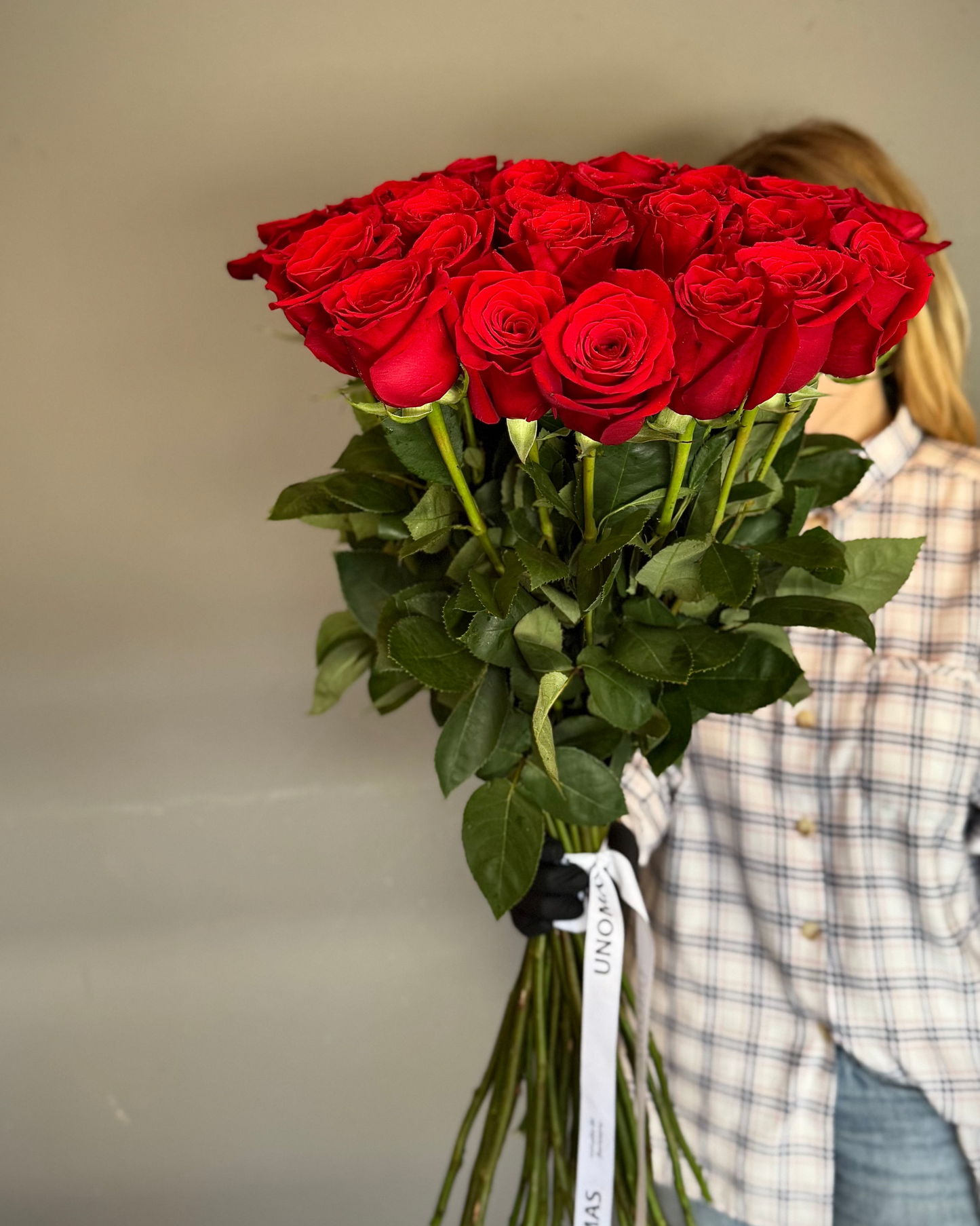 Person holding a large bouquet of red roses against a plain background