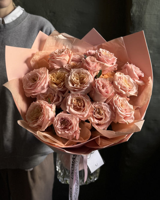 Bouquet of peach roses wrapped in peach paper held by a person.