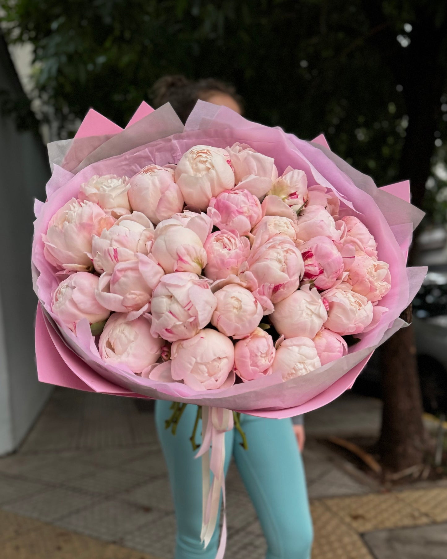 Person holding a large bouquet of pink peonies flowers