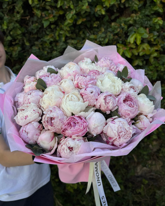 Bouquet of flowers peonies held by a person with a green bush background