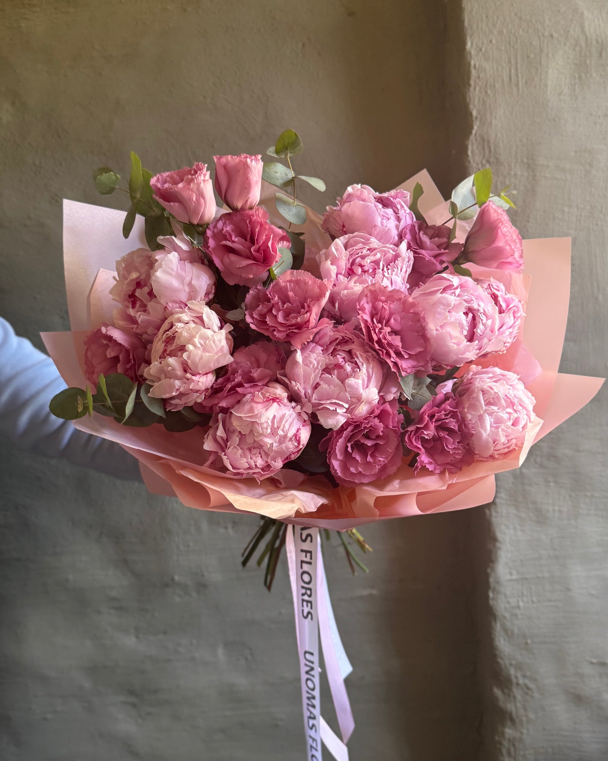 Bouquet of pink flowers peonies and alstroemeria held against a plain background
