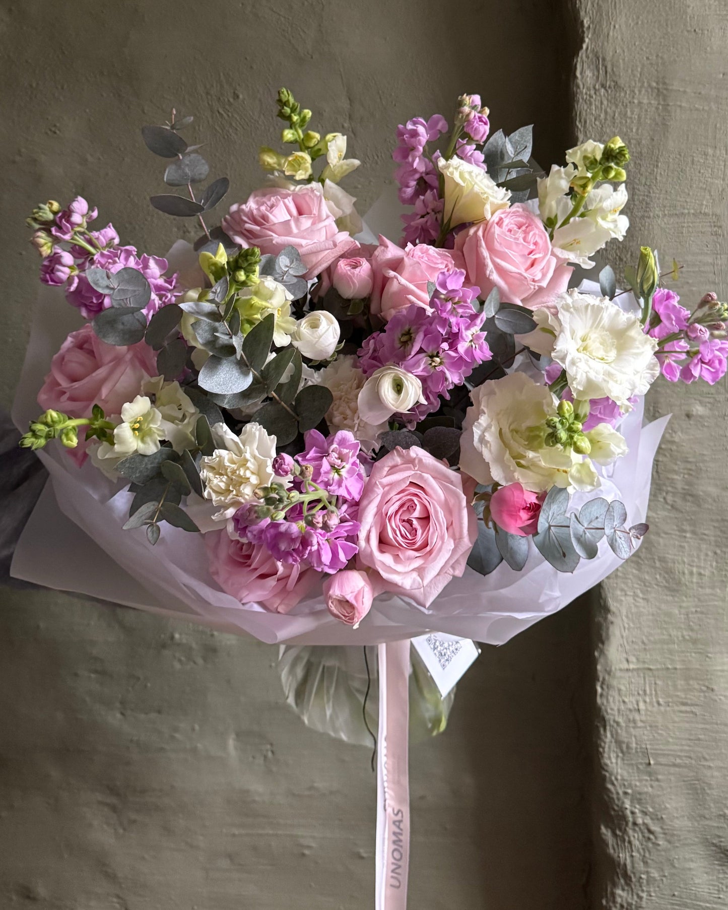 Bouquet of flowers wrapped in pink paper against a textured wall.