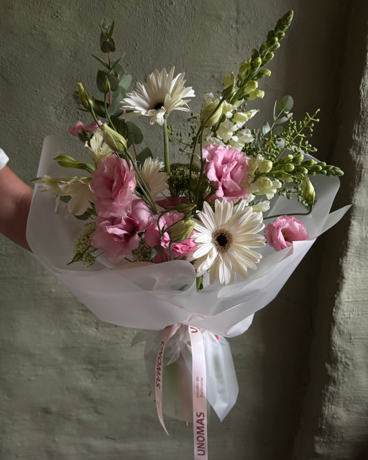 Bouquet of flowers wrapped in white paper with a ribbon against a textured wall.