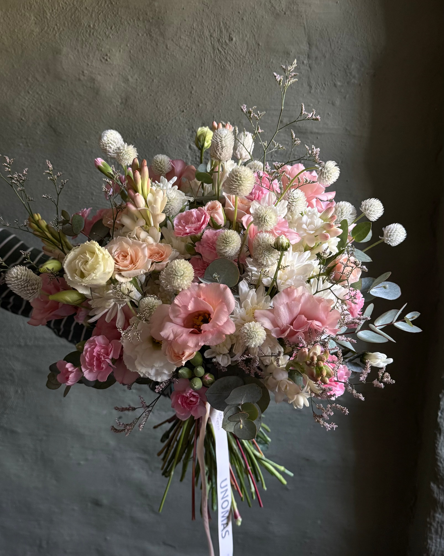 Bouquet of flowers with pink and white tones against a textured gray wall.